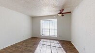 Located at 2510 Elmont Dr in Austin, TX, this single-story space offers a straightforward, functional layout with consistent finishes throughout. The living area features warm wood-look flooring that extends through the main spaces, white walls, and a textured popcorn ceiling. A pass-through window connects the living area to the kitchen, providing an open visual link between the two spaces while maintaining defined zones. Natural light filters in through a window fitted with horizontal blinds, and a ceiling fan with an integrated light fixture provides both airflow and overhead illumination.

The kitchen is efficiently designed with white cabinetry offering ample storage above and below the countertops, dark laminate counters, a double stainless steel sink, a coil-element electric range, and a refrigerator. An overhead range hood is positioned above the stove for ventilation.

The bedroom is a well-proportioned room with the same wood-look flooring, a prominent window that allows natural light to cast across the floor, and a ceiling fan matching the style found in the living area. The textured ceiling continues throughout, maintaining a cohesive aesthetic.

The bathroom includes a full tub and shower combination with white tile surround, a toilet, and a vanity with dark countertop and white cabinetry, all finished with wood-look flooring.