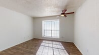 Located at 2510 Elmont Dr in Austin, TX, this single-story space offers a straightforward, functional layout with consistent finishes throughout. The living area features warm wood-look flooring that extends through the main spaces, white walls, and a textured popcorn ceiling. A pass-through window connects the living area to the kitchen, providing an open visual link between the two spaces while maintaining defined zones. Natural light filters in through a window fitted with horizontal blinds, and a ceiling fan with an integrated light fixture provides both airflow and overhead illumination.

The kitchen is efficiently designed with white cabinetry offering ample storage above and below the countertops, dark laminate counters, a double stainless steel sink, a coil-element electric range, and a refrigerator. An overhead range hood is positioned above the stove for ventilation.

The bedroom is a well-proportioned room with the same wood-look flooring, a prominent window that allows natural light to cast across the floor, and a ceiling fan matching the style found in the living area. The textured ceiling continues throughout, maintaining a cohesive aesthetic.

The bathroom includes a full tub and shower combination with white tile surround, a toilet, and a vanity with dark countertop and white cabinetry, all finished with wood-look flooring.