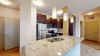 This single-floor residence offers a thoughtfully designed layout that balances modern finishes with functional living spaces. The kitchen serves as a central highlight, featuring rich dark-stained cabinetry extending to the ceiling, light granite countertops with subtle veining, and a full suite of stainless steel appliances including a refrigerator, electric range, and built-in microwave. A spacious island with an undermount double sink and elegant pendant lighting above adds both style and practicality to the space. Light hardwood-style flooring runs through the kitchen and living areas, lending warmth and continuity throughout. The living area is bright and open, benefiting from natural light that pours in through a large sliding glass door leading to an outdoor balcony. Two well-proportioned bedrooms are finished with plush neutral carpeting and windows that invite natural light. The unit includes two bathrooms: one featuring a walk-in glass-enclosed shower, granite vanity countertop, and dark wood cabinetry, and a second with a full soaking tub and shower combination, matching granite counters, and tile flooring. Clean, neutral wall tones and consistent trim details throughout create a cohesive and move-in ready aesthetic.