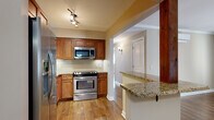 This single-floor residence offers a thoughtfully designed layout that balances functionality with a clean, modern aesthetic. Rich hardwood flooring runs throughout the main living areas, providing a warm and cohesive look.

The kitchen is a standout feature, outfitted with warm-toned wood cabinetry, granite countertops, and a full suite of stainless steel appliances including a refrigerator with ice maker, electric range, built-in microwave, and dishwasher. A classic subway tile backsplash adds texture and character, while a peninsula with a granite overhang connects the kitchen to the open living and dining area, making it ideal for both everyday living and entertaining.

The open-concept living and dining space is generously proportioned, featuring crown molding, a wall-mounted mini-split HVAC unit, and a pendant light fixture. A hallway leads to the private areas of the home, including a bedroom that benefits from natural light through double windows and is equipped with a ceiling fan.

The bathroom is finished with large-format tile flooring, a subway-tiled tub and shower surround, and a dark-toned vanity with a stone countertop, creating a clean and functional space. A distinctive natural wood post serves as an architectural accent at the kitchen-to-living transition, adding a unique design element throughout.