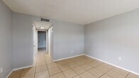 This single-story, 2-bedroom, 1-bathroom home offers a practical and efficient layout designed for comfortable everyday living. Light beige ceramic tile flooring runs consistently throughout the entire home, creating a cohesive and easy-to-maintain interior. The walls are painted in a neutral gray tone, lending a clean and modern feel to each room.

The living area greets you upon entry, featuring multiple windows that allow natural light to filter in and offer views of the surrounding greenery. A dedicated dining room provides a defined space for meals, while the kitchen is equipped with dark wood cabinetry, a tile backsplash, a range with overhead ventilation, and a full-size refrigerator — offering all the essentials in a compact, functional footprint.

Both bedrooms are modestly sized, each with windows that bring in natural light. The primary bedroom provides a comfortable retreat, and two closets throughout the home ensure adequate storage. The full bathroom includes a combined tub and shower with white tile surround, a toilet, and a vanity.

A hallway connects the main living spaces, and the home also features a centralized HVAC system with ceiling vents. An electrical panel is conveniently accessible within the unit. Overall, this home presents a straightforward, functional design well-suited for those seeking a manageable and practical living space.