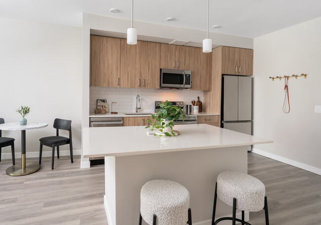 Finish Package II Kitchen with oak cabinetry, white quartz countertops, white tile backsplash, stainless steel appliances, pendant lighting, and hard-surface vinyl plank flooring - Avalon Westminster Promenade