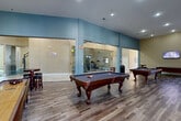 Located at 429 Valley St in Providence, Rhode Island, this impressive single-floor amenity center spans a generous footprint designed to accommodate a wide variety of recreational and social activities. The welcoming lobby greets visitors with large-format tile flooring, recessed lighting, comfortable seating arrangements, and glass-partitioned spaces that lend an open, airy feel throughout.

The game room is a standout feature, enclosed by floor-to-ceiling glass walls and furnished with multiple billiard tables and a foosball table, all set atop rich hardwood-style flooring. Adjacent to this is a cozy lounge area anchored by a dramatic full-height stone accent wall with a built-in fireplace, wall-mounted TV, and leather seating — a warm contrast to the more active spaces.

The dedicated fitness center is well-equipped with cardio machines, a multi-station weight system, and a wall-mounted TV, all within a carpeted, light-filled room. A full-size indoor basketball court with a Boston Celtics logo at center court and high ceilings adds a truly distinctive athletic amenity.

A fully appointed kitchen features white cabinetry, granite countertops, stainless steel appliances, and a central island. A private meeting room with large industrial-style windows and a round wood table rounds out this thoughtfully designed community space.