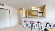 Located at 4300 Collegiate Way in Mount Pleasant, Michigan, this single-floor unit offers four bedrooms and two full bathrooms within a well-organized layout. The open-concept living and dining area is anchored by plush carpeting and natural light from large windows, with a sliding door in the living room providing access to an outdoor balcony area. The kitchen is positioned at the heart of the home, featuring light wood cabinetry, a raised breakfast bar with barstool seating, and essential appliances including a refrigerator, microwave, and dishwasher. A dedicated dining area adjacent to the kitchen accommodates a full-sized table, making it ideal for group meals. A standout practical feature is the in-unit stacked washer and dryer, conveniently located within the kitchen area alongside wood-look flooring. Each bedroom is carpeted and includes a closet and window, offering comfortable, functional spaces suitable for studying and resting. The bedrooms are well-proportioned, with the primary bedroom providing a generous footprint. The two bathrooms are finished with tile flooring, light wood vanities, and a full tub-shower combination. Overall, the unit provides a functional and comfortable living environment well-suited for shared occupancy near Central Michigan University.