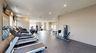 Located at 4100 Lakeview Crossing in Columbus, Ohio, this well-appointed fitness center offers a generous, open layout designed to accommodate a full range of workout activities. The single-floor space is bathed in natural light streaming through large windows fitted with horizontal blinds, creating a bright and energizing environment throughout the day. Ceiling fans are positioned strategically across the room to maintain comfortable air circulation during workouts.

The cardio zone is prominently featured, housing a row of modern treadmills each equipped with individual digital displays and mounted flat-screen televisions overhead for entertainment. Alongside the treadmills, elliptical trainers and stationary bikes provide additional low-impact cardio options. A dedicated strength training area includes a multi-station cable machine and a leg press unit, while a free weight section offers a full rack of dumbbells and a wall of mirrors to support proper form.

The flooring consists of durable dark rubberized material suited for high-traffic fitness use. Recessed lighting complements the natural light from the windows. The space also includes an open stretching and functional training area with ample floor space. An emergency exit, fire extinguisher, and safety postings reflect a commitment to safety. The overall ambiance is clean, modern, and welcoming, making it a practical and well-equipped community fitness facility.