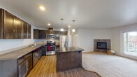 This single-floor residence offers a thoughtfully designed open-concept layout that seamlessly connects the kitchen and living areas. The kitchen is a functional standout, featuring dark espresso-stained cabinetry, a full suite of stainless steel appliances including a gas range, microwave, dishwasher, and refrigerator, as well as a central island with a dark countertop and bar seating. Warm wood-look flooring runs throughout the kitchen and main living area, while pendant lighting above the island adds a refined touch. The spacious living room transitions naturally from the kitchen and is highlighted by a tile-surround fireplace, providing a welcoming focal point. A wall-mounted mini-split unit ensures year-round climate comfort, and a glass-paneled door offers access to the exterior. The bedrooms are generously sized with plush carpeting and windows fitted with horizontal blinds that allow natural light while maintaining privacy. The bathroom is clean and practical, featuring dark vanity cabinetry, a countertop sink, a large mirror, and wood-look vinyl flooring. Throughout the residence, neutral tones and consistent finishes create a cohesive, modern aesthetic that is both functional and inviting.