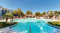 Located at 5150 N 99th Ave in Phoenix, Arizona, this outdoor amenity space presents a resort-caliber pool environment designed for relaxation and recreation in the heart of the Sonoran Desert. The centerpiece is a generously sized freeform swimming pool with striking turquoise water, accented by decorative blue tile detailing along the pool floor. The organic, curving shape of the pool creates an inviting, resort-like atmosphere that extends across a spacious concrete pool deck.

Throughout the deck, multiple landscaped islands break up the hardscape, featuring palm trees, native desert plantings, manicured shrubs, and decorative boulders that reinforce the Arizona aesthetic. Lounge chairs are positioned around the perimeter, offering ample space for sunbathing under the abundant Phoenix sunshine.

A covered pavilion with a clay tile roof and arched entryways serves as a central gathering hub, providing shade and a communal space adjacent to the pool. Stone-clad pillar accents and wrought iron fencing frame the space, adding architectural character. Mature shade trees line the outer boundary, offering a natural privacy screen. The surrounding multi-story residential buildings with Spanish-influenced architecture complete the enclosed, community-focused setting.