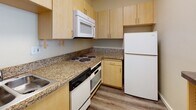 Located at 609 Broadway in the heart of Santa Monica, CA, this single-floor unit offers a practical and well-organized layout designed for comfortable urban living. The living area is bright and open, featuring durable wood-style flooring and a large sliding glass door fitted with vertical blinds that invites an abundance of natural light and provides views of the surrounding cityscape. A built-in wall unit with light wood cabinetry, open shelving, and integrated drawers offers generous storage and display space, complementing the overall aesthetic of the room. The kitchen is efficiently designed with light maple cabinetry, granite-style countertops, and a full suite of white appliances including a refrigerator, range, built-in microwave, and dishwasher. A peninsula counter serves as a natural divider between the kitchen and living space. The bathroom is appointed with a granite-topped vanity, light wood cabinetry with brushed nickel hardware, a large mirror, and a glass-enclosed shower. Closet space is provided with a rod and shelving system ideal for organized storage. The warm, neutral color palette and consistent wood-style flooring throughout create a cohesive and inviting atmosphere in this well-situated Santa Monica residence.