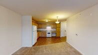 Located on Second St NW in downtown Canton, Ohio, this well-appointed one-bedroom, two-bathroom residence offers a thoughtfully designed open-concept layout with modern finishes throughout. The combined kitchen and living area serves as the heart of the unit, showcasing light-toned hardwood-style flooring, recessed lighting, and a ceiling fan. A bank of large windows with roller shades fills the living space with natural light and frames sweeping views of the Canton cityscape. The kitchen features a peninsula with granite countertops and bar seating, cream cabinetry, a white subway tile backsplash, stainless steel appliances, and stylish pendant lighting overhead. A hallway connects the main living area to the private bedroom, which is carpeted for comfort and includes a built-in closet organizer and ceiling fan. The primary bathroom is generously sized, offering a double-sink vanity with granite countertops, dark wood cabinetry, a large glass-enclosed walk-in shower, and a wall-length mirror. A second bathroom provides additional convenience. Neutral wall tones and clean architectural lines give the space a cohesive, contemporary feel throughout.