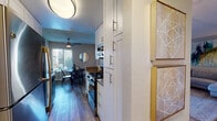 This single-floor residence offers a thoughtfully designed layout that balances comfort and functionality across its key living spaces. The galley-style kitchen is equipped with white shaker cabinetry featuring brushed nickel hardware, a gas range, stainless steel appliances, and warm wood-tone flooring that extends into the adjacent dining area. The dining space is brightened by a large window with outdoor views and is accented by a bold piece of wall art, creating an inviting atmosphere for everyday meals. The living room is generously proportioned, featuring wood-style flooring, a textured ceiling, and warm ambient lighting that lends the space a cozy, welcoming feel. Two bedrooms provide comfortable retreats; the primary bedroom includes a mirrored sliding closet, plush carpeting, and a textured ceiling, while the second bedroom features carpet flooring, natural light from a window with blinds, and ample room for furnishings. The primary bathroom offers a vanity with stone-look countertops, white cabinetry, and a separate walk-in shower with glass enclosure. A second full bathroom includes a tub-shower combination and wood-look flooring. Throughout the residence, neutral tones and consistent finishes create a cohesive, modern aesthetic.