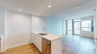 Located at 955 Eleventh Avenue in San Diego's vibrant Columbia District, this contemporary 1-bedroom, 1-bathroom residence offers a thoughtfully designed single-level layout with a clean, modern aesthetic throughout. Light-toned hardwood flooring runs seamlessly across the main living areas, complementing the bright, neutral palette of white walls and crisp trim.

The open-plan kitchen and living area serves as the heart of the home. The kitchen is outfitted with white flat-front cabinetry, a tiled backsplash, stainless steel appliances including a French door refrigerator, electric range, microwave, and dishwasher, and a generous island with a quartz countertop and undermount sink — ideal for both cooking and casual dining. Recessed lighting adds to the polished finish.

The living area is bathed in natural light through expansive floor-to-ceiling windows and glass doors that frame sweeping views of the San Diego skyline, lending an airy, elevated feel to the space.

The bedroom continues the floor-to-ceiling window theme, offering additional city views and access to a private balcony. A mirrored sliding-door closet provides practical storage. The bathroom features large-format tile flooring, a white vanity with an undermount sink, a mirror with integrated lighting, and a tub-shower combination with marble-style tile surround.