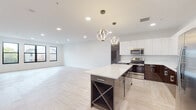 This contemporary single-floor residence showcases a thoughtfully designed open-concept layout that seamlessly integrates the living and kitchen areas. The herringbone-patterned light wood flooring flows throughout the main living space, creating a warm yet sophisticated aesthetic. Recessed lighting and large black-framed windows allow natural light to fill the generously proportioned living area, which also features an exposed ductwork detail that adds an industrial-modern touch.

The kitchen is a standout centerpiece, outfitted with two-tone cabinetry — high-gloss white upper cabinets paired with deep espresso lower cabinets — complemented by white quartz countertops and a matching backsplash. A large island with built-in wine storage anchors the space, while a pair of sculptural pendant lights add elegance overhead. Stainless steel appliances complete the culinary suite.

The bedroom opens directly to a private balcony through sliding glass doors, offering outdoor views of the surrounding neighborhood and abundant natural light, with a ceiling fan adding comfort.

The bathrooms are finished to a high standard, featuring large-format marble-look porcelain tile, a floating dual-sink vanity with backlit mirrors, and a glass-enclosed shower, combining clean lines with a luxurious ambiance throughout.