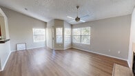 This single-story home offers a thoughtfully designed layout with a variety of distinct living spaces, each finished with care and attention to detail. The main living area is bright and open, featuring light hardwood-style flooring, vaulted ceilings, and multiple large windows fitted with blinds that allow generous natural light to fill the room. A ceiling fan adds both function and style overhead, while a textured ceiling provides a classic finishing touch throughout. A secondary living or dining area showcases a tile-surround wood-burning fireplace as its focal point, accompanied by additional windows and another ceiling fan, creating a warm and inviting atmosphere. Sliding glass doors with vertical blinds provide access to the exterior, enhancing the connection between indoor and outdoor spaces. The kitchen is well-equipped with rich wood cabinetry, dark granite countertops, a double-basin sink, and black appliances including a range, microwave, dishwasher, and refrigerator, all set atop hardwood-style flooring. The bedrooms offer a quieter retreat, finished with plush carpeting, neutral walls, and windows that bring in soft natural light. The overall palette of warm neutrals and natural materials gives the home a clean, cohesive, and comfortable feel throughout.