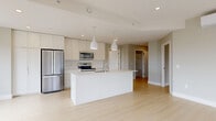 This well-appointed 3-bedroom, 2-bathroom unit at 49 Brookline Drive in Halifax, Nova Scotia, offers a thoughtfully designed open-concept layout with a clean, contemporary aesthetic throughout. The combined kitchen and living area serves as the heart of the home, anchored by a large central island with an undermount sink and pendant lighting overhead. White cabinetry extends to the ceiling, complemented by a tile backsplash and a full suite of stainless steel appliances, including a French door refrigerator, electric range, and built-in microwave. Light-toned hardwood-style flooring runs throughout, enhancing the bright and airy feel of the space. The generously sized primary bedroom features large windows with roller shades and outdoor views, alongside a spacious walk-in closet with built-in shelving. Two additional bedrooms offer versatile use, each finished with the same light flooring and neutral tones. Both bathrooms are finished with tile flooring, white vanities, and large mirrors. A dedicated laundry room houses a full-sized washer and dryer. The private balcony, framed by glass railings, overlooks a natural treed landscape, offering a peaceful outdoor retreat. This unit combines functional design with modern finishes in a serene Halifax setting.