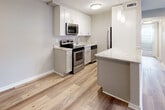 Located at 1710 Devonshire Rd in Hauppauge, NY, this single-floor residence combines modern updates with a warm, neutral palette to create a comfortable and cohesive living environment. The main living area features light-toned hardwood-style flooring, recessed lighting, and a large sliding glass door that floods the space with natural light and provides direct outdoor views. Elegant French doors with glass panel inserts connect the living area to an adjacent room, adding architectural character and an open, airy feel. The kitchen is well-appointed with stainless steel appliances, white upper cabinetry, grey lower cabinetry, marble-look countertops, and pendant lighting, all set over light hardwood-style flooring. A kitchen island extends the counter space and adds a functional dining element. The bedrooms are carpeted and feature ceiling fans, natural light from windows with blinds, and generous closet space, including sliding and paneled closet doors. The bathroom is finished with large-format neutral stone-look tile surrounding a soaking tub and tub-shower combination, complemented by chrome fixtures for a clean, modern look. Throughout the home, a consistent soft grey and beige color scheme, white trim, and updated finishes create a polished and move-in ready atmosphere.