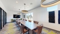 This thoughtfully designed co-working space combines a professional conference area with a dedicated workstation nook, offering a versatile environment for meetings and focused work. The single-floor layout is efficiently organized, with a large rectangular boardroom table at its center, surrounded by leather upholstered chairs accommodating a sizeable group. Overhead, a series of bold circular pendant lights provide warm, even illumination throughout the space.

Floor-to-ceiling glass panels and large windows along one wall allow generous natural light to pour in, offering exterior views that enhance the open, airy atmosphere. A wall-mounted flat-screen display at one end of the conference area supports presentations and collaborative work sessions.

At the rear of the space, a dedicated workstation area features dual computer desks set against a striking full-wall forest mural, creating an immersive, nature-inspired backdrop. Textured wall art panels in deep blue tones and a collection of organic wood sculptures mounted on the walls add curated visual interest throughout.

The patterned carpet in muted grey and yellow tones ties the design together, while black-framed glass doors connect the space to adjoining areas. The overall ambiance is modern, professional, and distinctly design-forward.