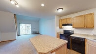 This two-story residence is thoughtfully designed to maximize both functionality and openness. The main level centers around an open-concept kitchen and living area, where warm honey-toned wood cabinetry pairs with granite-look countertops on a central island that doubles as a breakfast bar. Black appliances, including a range with overhead ventilation, dishwasher, and refrigerator, complement the kitchen's practical layout. The kitchen transitions seamlessly between hardwood-style flooring and plush carpeting as it opens into the living area, which is anchored by a sliding glass door leading to a private balcony with outdoor views. A wall-mounted HVAC unit provides climate control on this level.

A wood-railed staircase leads to the upper loft level, where vaulted ceilings rise dramatically and a ceiling fan adds comfort to the generously sized space. The upper floor also includes a carpeted bedroom with a double-door closet offering ample hanging and storage space, as well as a full bathroom featuring a single-sink vanity with wood cabinetry, a large wall mirror, and a tub-shower combination. Throughout the home, neutral tones and warm wood trim details create a cohesive and inviting atmosphere.