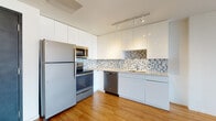 Located at 144 S Harrison St in East Orange, NJ, this thoughtfully designed single-floor residence combines modern finishes with functional living spaces throughout. The kitchen serves as a standout feature, showcasing high-gloss white cabinetry extending to the ceiling, a mosaic tile backsplash, light countertops, and a full suite of stainless steel appliances including a refrigerator, electric range, built-in microwave, and dishwasher. Track lighting overhead provides excellent task illumination, while warm hardwood-style flooring ties the space together seamlessly. The open living area is bathed in natural light through large picture windows that frame expansive views of the East Orange skyline and surrounding greenery, creating a bright and airy atmosphere. The bedroom offers similar large windows with sweeping outdoor views and features a double-door closet for generous storage. A dedicated in-unit laundry area with a stacked washer and dryer adds everyday convenience. The bathroom is finished with large-format tile flooring, a modern vanity, and clean, minimalist fixtures. Clean white walls, contemporary doors, and consistent flooring throughout lend the space a cohesive, move-in-ready aesthetic.