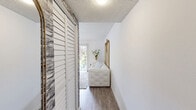 Located at 6919 Bonair Drive in Tampa, FL, this thoughtfully designed single-story, one-bedroom, one-bathroom home offers a cohesive and refined aesthetic throughout. The open living room is bright and airy, featuring wood-look flooring, large sliding glass doors with vertical blinds that invite natural light, and a clean white palette accented by ornate gold-framed mirrors. The space flows seamlessly into a separate dining area, where a striking crystal chandelier hangs above a glass-top table with white upholstered chairs, complemented by patterned window treatments and wainscoting details. The kitchen is well-equipped with white shaker cabinetry, granite-look countertops, and an eye-catching stacked stone accent wall that continues into the hallway. A stacked washer and dryer unit is conveniently integrated into the kitchen area. The bedroom offers a warm contrast, showcasing a textured stone accent wall, rich dark wood furniture, and ample closet space. The full bathroom features a tub-shower combination, white tile surround, and a granite-topped vanity. Throughout the home, wood-look flooring, textured ceilings, and carefully chosen accents create a polished, inviting atmosphere.