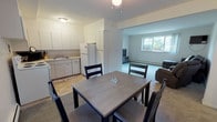 This two-bedroom, one-bathroom unit in Ann Arbor, Michigan offers a well-organized single-floor layout designed for comfortable everyday living. The kitchen is outfitted with white cabinetry, ample counter space, a double sink, a white refrigerator, and a range, providing a clean and functional cooking environment with tile flooring underfoot. Adjacent to the kitchen, the dining area accommodates a four-seat table and benefits from a window that frames views of surrounding greenery, bringing natural light into the space. The living room flows naturally from the dining area and features plush carpeting, a wall-mounted television, and a large window overlooking the outdoors, creating a relaxed and inviting atmosphere. Both bedrooms are carpeted and modestly sized, each with windows that allow natural light and exterior views. The primary bedroom offers space for a full-size bed and a nightstand, while the second bedroom comfortably fits twin beds alongside shared furniture. The full bathroom is finished with tile flooring, a shower-tub combination, a single vanity with under-sink cabinetry, and a window for ventilation. Baseboard heating is present throughout the unit, and the neutral color palette lends a clean, understated aesthetic to the overall space.