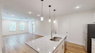 Located at 11122 Hambright Junction Drive in Huntersville, NC, this well-appointed single-floor residence offers three bedrooms, two bathrooms, and a thoughtfully designed open layout. The kitchen is a standout feature, showcasing crisp white cabinetry reaching to the ceiling, granite countertops, stainless steel appliances including a range and built-in microwave, and a large island with a sink — all set atop warm hardwood-style flooring that flows throughout the home. Recessed lighting and pendant fixtures keep the space bright and functional. The living area connects seamlessly to the kitchen, creating an inviting open-concept environment. The bedrooms are bright and airy, with several featuring transom-topped doors opening to a private balcony that overlooks a lush, tree-lined backdrop — providing a serene natural setting. The primary bedroom includes direct access to an en-suite bathroom. Both bathrooms are finished with granite-topped vanities and clean white tile, with one featuring a full tub-shower combo accented by subway tile. Closets are equipped with wire shelving systems for organized storage. The home's neutral palette, consistent flooring, and modern hardware give it a cohesive, move-in-ready aesthetic throughout.