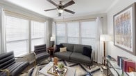 This single-floor residence offers a thoughtfully designed layout that balances comfort and functionality. The kitchen is a standout space, featuring rich dark espresso cabinetry, a glass subway tile backsplash, stainless steel appliances including an electric range and French door refrigerator, and a light quartz island with an undermount sink. Crown molding and track lighting add refined detail to the kitchen and adjoining dining area. The dining space accommodates a round glass table and benefits from natural light through a window dressed with white blinds and sheer curtains. The living room is generously sized and bathed in natural light from multiple large windows, each fitted with wood blinds and white drape panels. A ceiling fan enhances the room's airy feel, and durable hardwood-style flooring runs throughout the common areas. The primary bedroom features plush carpeting, a ceiling fan, and a natural light source from a well-positioned window. The second bedroom is equally comfortable, also finished with carpet and a ceiling fan. Two full bathrooms serve the residence — one with a dark vanity, white quartz countertop, and a tub/shower combination with classic white subway tile, and another featuring an arched architectural detail framing the tub surround, adding a distinctive design touch.