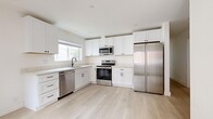 This single-story home offers an efficiently arranged floor plan with 5 bedrooms, 2 full bathrooms, a kitchen, and two hallways connecting the living spaces. Light-toned hardwood flooring runs consistently throughout, creating a cohesive and airy feel across every room.

The kitchen is a standout feature, outfitted with crisp white shaker cabinetry, stone countertops, and a full suite of stainless steel appliances including a refrigerator, range, built-in microwave, and dishwasher. A window above the sink brings in natural light, enhancing the clean, modern aesthetic.

Each of the five bedrooms maintains a minimalist design with white walls, light wood flooring, and individual windows that provide natural light and outdoor views of surrounding greenery. The bedrooms vary in size, with the primary bedroom offering a comfortable footprint suited for a full bedroom setup.

Both bathrooms share a consistent design language — white cabinetry, stone-topped vanities, tiled tub-shower combinations, and matte black fixtures that provide a modern contrast. Natural light enters through high windows, keeping the spaces bright and open.

A common area with a glass-panel exterior door provides access to the outdoors and additional natural light. Throughout the home, the neutral white palette, modern finishes, and consistent flooring create a clean and functional living environment.