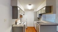 This single-floor residence offers a functional and well-organized layout designed for comfortable everyday living. The galley-style kitchen is a standout feature, lined on both sides with gray cabinetry providing ample storage, granite-style countertops, and white appliances including a coil-burner range, refrigerator, and dishwasher. Warm hardwood-style flooring runs the length of the kitchen, adding a touch of warmth to the neutral color palette. The kitchen opens toward the living area via a half-wall counter, creating a connected, open feel. The living area is carpeted and bathed in natural light from a sliding glass door fitted with vertical blinds, which leads to an outdoor space with views of surrounding greenery. A ceiling fan keeps the space comfortable year-round. The bedrooms are carpeted and feature ceiling fans with light fixtures, along with windows dressed in blinds that allow natural light while maintaining privacy. The bathroom is equipped with a dual-sink vanity topped with granite-style countertops, framed mirrors, and bright vanity lighting. Throughout the unit, textured ceilings, neutral wall tones, and consistent finishes contribute to a cohesive and practical living environment.
