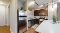This thoughtfully designed two-bedroom, one-bathroom residence offers a comfortable and efficient single-level layout. The kitchen serves as a standout feature, showcasing rich dark wood cabinetry, a classic white subway tile backsplash, stainless steel appliances including a refrigerator, range, microwave, and dishwasher, and a large center island with a light quartz countertop. Pendant lighting and a track lighting system illuminate the space stylishly, while warm hardwood-style flooring extends throughout the kitchen and main living areas. A hallway connects the main living space to the private quarters, where both bedrooms are finished with plush wall-to-wall carpet, ceiling fans, and windows that invite natural light. The primary bedroom offers a comfortable footprint with outdoor tree views. The bathroom features hardwood-style tile flooring, a tub-shower combination, and direct access to a dedicated closet with built-in shelving for ample storage. Neutral wall tones throughout create a clean, versatile backdrop. The layout flows logically from the open kitchen and living area through the hallway to the bedrooms and bathroom, making efficient use of every square foot in this well-organized residence.