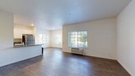 This single-floor unit is designed with a clean, contemporary aesthetic and a functional open-concept layout. The living area is bright and spacious, featuring rich wood-style hard flooring that extends throughout the main living spaces. Multiple windows fitted with horizontal blinds allow generous natural light to fill the room while framing outdoor views of surrounding trees. A wall-mounted HVAC unit provides climate control directly within the living area.

The kitchen is well-appointed and open to the living space, anchored by a central island with a grey countertop and an integrated sink, offering both prep space and a casual dining area. White shaker-style cabinetry lines the walls, complemented by stainless steel appliances including a refrigerator, gas range, and microwave. Recessed lighting overhead adds a modern touch.

The bedrooms are carpeted for comfort and finished with neutral white walls, providing a calm and restful atmosphere. Each room features clean lines, standard closet access, and windows that bring in natural light. The overall palette throughout the unit is neutral and understated, creating a versatile backdrop that suits a variety of uses.