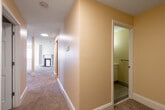 This single-floor unit offers a thoughtfully arranged layout with a variety of architectural details that lend it considerable character. The standout feature is a generously sized curved living area, where a sweeping curved wall lined with multiple windows allows natural light to pour in from multiple angles, creating a bright and airy atmosphere. Carpet flooring flows throughout the main living spaces, complementing the warm, neutral palette of cream and beige tones on the walls.

A decorative fireplace with a classic white mantle serves as a focal point in the main living space, adding a traditional touch. Adjacent to the living area, a hallway leads to the remaining rooms, including a bedroom distinguished by a full exposed brick accent wall — a nod to the building's historic character — paired with carpeted flooring and a double-hung window.

The kitchenette features light oak cabinetry, a laminate countertop, stainless steel sink, and hardwood flooring, providing practical functionality in a compact footprint. The bathroom is straightforward and clean, equipped with a tiled shower, toilet, single-basin vanity with under-cabinet storage, and tile flooring. The corridor connecting the rooms is lined with carpet and provides clear sightlines throughout the unit.