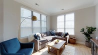 Located at 1414 Broadview Ave in the heart of Columbus, Ohio, this single-floor residence offers a thoughtfully designed layout that balances comfort and style. The living area is a standout feature, bathed in abundant natural light streaming through multiple large windows dressed with clean horizontal blinds. Crown molding adds a refined architectural touch, while light hardwood flooring grounds the space with warmth and continuity. The room comfortably accommodates generous seating, making it well-suited for both relaxed everyday living and casual entertaining. A modern arc floor lamp with a brushed gold finish provides an elegant ambient lighting option, complementing the neutral, contemporary color palette throughout. The overall ambiance of the home is bright, airy, and inviting, with a calm and cohesive aesthetic that carries through the space. Situated in Columbus's established Grandview Heights area, the property benefits from a desirable location with convenient access to local amenities, dining, and community spaces. This single-story layout offers ease of movement and accessibility, making it a practical and appealing option for a wide range of occupants.