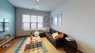 Located at 29 E Green St in Champaign, IL, this modern single-floor unit offers a well-designed layout ideal for comfortable urban living. The kitchen is a standout feature, boasting sleek gray cabinetry, stainless steel appliances including a full-size refrigerator, electric range, and microwave, complemented by a light quartz countertop island, subway tile backsplash, and light hardwood-style flooring. Track lighting and a stylish pendant fixture add both function and flair to the space. The living area is bright and open, with large windows that allow ample natural light and views of the surrounding cityscape. Hardwood-style flooring continues throughout, lending a cohesive, contemporary feel. The space includes multiple bedrooms, each featuring carpeted floors, generous windows with blinds, and sufficient room for a bed and desk setup — well-suited for students or young professionals. Two bathrooms mirror the modern aesthetic of the unit, with gray cabinetry, quartz-style vanity countertops, light hardwood-style flooring, and clean neutral walls. One bathroom features a glass-enclosed shower. Throughout the unit, the neutral gray and white color palette, modern fixtures, and consistent finishes create a clean, functional, and inviting atmosphere.