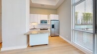 Located at 1150 4th St SW, Unit 320 in Washington, DC, this one-bedroom, one-bathroom residence offers a well-designed layout with a clean, modern aesthetic throughout. Light hardwood flooring runs continuously across the open living areas, complementing the bright, white walls and creating a cohesive, airy feel.

The kitchen is a standout feature, equipped with white cabinetry, stainless steel appliances including a side-by-side refrigerator and built-in microwave, a granite-topped island on casters, and a subway tile backsplash. A tray ceiling above the kitchen adds architectural definition to the space. Tall windows allow natural light to pour in alongside the kitchen area.

The living area benefits from dramatic floor-to-ceiling windows that frame views of the surrounding neighborhood and greenery, filling the space with abundant natural light. The bedroom is a comfortable, well-proportioned room with its own generous window, light hardwood floors, and crisp white walls.

The bathroom features a granite-topped vanity with a dark wood base, a tiled tub-shower combination, and clean white tile work throughout. Two hallways and a dedicated closet provide practical storage and circulation. Exposed concrete accents in the hallway add an industrial touch that contrasts tastefully with the otherwise polished interior finishes.