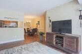 Located at 200 Red Cedar Ct in Chesapeake, Virginia, this single-floor residence offers a well-organized layout with a cohesive, warm aesthetic throughout. The living area features rich hardwood flooring and flows seamlessly into a dedicated dining room, which is distinguished by classic wainscoting, a chandelier, and a glass-top dining table — a refined setting for everyday meals or entertaining. The galley-style kitchen is outfitted with warm oak cabinetry, stainless steel appliances including a gas range and refrigerator, and ample counter space, with a convenient passthrough to the adjacent laundry area. The bedrooms are carpeted and filled with natural light from large windows with sheer curtains. One bedroom serves capably as a home office, featuring its own window with outdoor views and generous floor space. The bathroom includes warm wood cabinetry, a tub-shower combination, and hardwood flooring, offering both function and comfort. Neutral wall tones in soft beige and cream are carried throughout the home, creating a calm, cohesive atmosphere. The floor plan, as seen in the dollhouse view, reveals an efficient and thoughtfully connected layout that maximizes the use of every room.