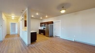 Located at 16511 East Sprague Avenue in Spokane Valley, Washington, this single-floor unit offers a thoughtfully designed layout with a seamless flow between living and kitchen spaces. The open-concept main area features warm wood-look laminate flooring throughout, with a partial wall divider elegantly separating the living room from the kitchen. The kitchen is well-appointed with rich dark-stained cabinetry, stainless steel appliances including a refrigerator, range, and microwave, complemented by light countertops and recessed lighting overhead. Pendant lights above the kitchen pass-through add a modern decorative touch.

The unit includes two bedrooms, each finished with plush carpeting, neutral-toned walls, and baseboard heating. Natural light enters through windows offering views of the surrounding neighborhood. The two bathrooms are finished with tile-look flooring, dark vanity cabinetry, mosaic tile backsplash accents, and wide mirror panels. One bathroom features a full soaking tub and shower combination with built-in shelving. Additional conveniences include in-unit laundry hookups. The overall design maintains a clean, modern aesthetic with consistent neutral tones and quality finishes throughout.