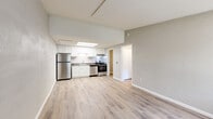 This single-floor unit offers a clean, modern layout with an open-concept design that connects the kitchen and living area seamlessly. The kitchen is well-equipped with stainless steel appliances, including a refrigerator, electric range, and dishwasher, complemented by crisp white cabinetry, dark granite-style countertops, and a skylight overhead that fills the space with natural light. Light hardwood-style flooring runs throughout the unit, creating a cohesive and bright aesthetic.

The living area is generously proportioned, offering flexible space for various furniture arrangements. A bedroom features a large window with vertical blinds and a built-in under-window cabinet unit, allowing for ample natural light. An additional bedroom or flex room also benefits from a window overlooking a tree-lined exterior.

The bathroom includes a full-size tub and shower combo with chrome fixtures and a clean, neutral finish. A dedicated utility area houses a full-size water heater, providing practical in-unit utility access. Throughout the unit, neutral gray tones on the walls, white trim, and consistent flooring contribute to a bright, cohesive, and move-in-ready living environment.