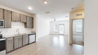 Located at 1050 Old Gilliard Rd in Ridgeville, SC, this single-story, one-bedroom, one-bathroom home offers a thoughtfully designed layout with modern finishes throughout. The kitchen is a standout feature, equipped with stainless steel appliances including a refrigerator, range, microwave, and dishwasher, all complemented by warm wood-tone cabinetry, granite-look countertops, a tile backsplash, and light wood-style flooring. The open living area flows naturally from the kitchen, bathed in natural light from large windows and a sliding glass door, and is topped with a ceiling fan for added comfort. The bedroom is carpeted for warmth and comfort, features a ceiling fan, and receives ample natural light through a window. The bathroom is finished with a wood-tone vanity, granite-look countertop, a large mirror, and accessibility grab bars. A dedicated laundry area accommodates a full-size washer and dryer side by side. Additional spaces include a hallway, closet, and consistent light wood-style flooring in the common areas, creating a cohesive and clean aesthetic throughout this well-appointed home.