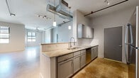 This urban loft-style residence offers a thoughtfully designed two-bedroom, one-bathroom layout that blends industrial character with modern finishes. Polished concrete floors run throughout the entire space, reflecting natural light and lending a sleek, contemporary feel. Exposed metal ductwork and pipes trace the ceilings, reinforcing the industrial aesthetic, while track lighting and ceiling fans provide both function and style.

The open-concept living area is generously proportioned, with multiple windows allowing natural light to pour in from multiple angles. The kitchen is a standout feature, centered around a peninsula with granite countertops, gray shaker-style cabinetry, a white subway tile backsplash, and a full suite of stainless steel appliances including a refrigerator, range, microwave, and dishwasher. Pendant lighting above the peninsula adds a refined touch.

The spacious primary bedroom offers ample room for a full furniture arrangement, benefiting from natural light and a ceiling fan overhead. The bathroom is elegantly finished with a dual-sink vanity featuring gray cabinetry and white countertops, complemented by a full tub and shower adorned with marble-style tile surround. A dedicated in-unit laundry area and a closet complete the practical amenities of this distinctive urban residence.
