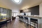 Located at 3850 Coleman Rd in East Lansing, Michigan, this single-floor unit offers four bedrooms and four bathrooms within a well-designed, functional layout. The open-concept common area seamlessly connects the kitchen, dining, and living spaces, creating a cohesive and social environment. The kitchen is outfitted with dark cabinetry, granite countertops, stainless steel appliances — including a range, microwave, refrigerator, and dishwasher — and a breakfast bar with seating for multiple guests. A decorative green accent wall adds character to the dining area, while the living room benefits from a glass door and large windows that invite natural light and provide outdoor views. Hardwood-style flooring runs throughout the main living areas, lending a clean and modern aesthetic. Each of the four bedrooms features carpeted floors and a sliding-door closet, with the primary bedroom offering additional space for a desk and work area. The bathrooms are finished with tub-shower combinations in a clean, neutral palette. An in-unit laundry area with a washer and shelving provides everyday convenience. The overall ambiance is modern and functional, well-suited for shared living.