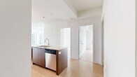 Located on a high floor at 320 Tweedsmuir Ave in Toronto's Forest Hill neighbourhood, this 2-bedroom, 1-bathroom unit offers a bright and contemporary open-concept layout finished with light hardwood flooring throughout. The expansive living area is anchored by floor-to-ceiling windows that wrap around the space, flooding it with natural light and framing panoramic views of the city skyline and surrounding treetops. A sleek, modern kitchen features warm wood cabinetry, stainless steel appliances including a full-size refrigerator and range, a tiled backsplash, and a generous island with a double sink and light stone countertops — ideal for both everyday living and entertaining. Both bedrooms are well-proportioned, each with large windows and mirrored sliding closet doors that enhance the sense of space. The primary bedroom offers a tranquil view overlooking lush greenery below. The bathroom is finished with white subway tile, an accent band of earthy mosaic tile, and a soaker tub with overhead rain shower. Clean white walls, consistent flooring, and a neutral palette throughout lend the unit a cohesive, modern aesthetic.
