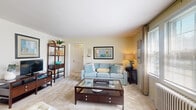 Located at 100 Forest Park in Portland, Maine, this two-bedroom, one-bathroom single-floor residence offers a well-organized layout across a compact but thoughtfully arranged floor plan. The living room serves as the central gathering space, featuring plush carpet flooring, large windows that invite abundant natural light, and enough room for multiple seating arrangements. A glass-topped coffee table and open shelving add functional character to the space.

The kitchen is efficiently designed with white cabinetry trimmed in warm wood accents, a stainless steel sink, coil-top range, and full-size refrigerator — providing all essential appliances in a tidy galley-style configuration.

The primary bedroom features soft carpet flooring, a calming teal accent wall, and dual windows with natural light, creating a restful retreat. The second bedroom is cozy and versatile, with a window dressed in bold red curtains, built-in desk space, and a radiator — ideal as a guest room or home office.

A connecting hallway links the rooms with ease. The full bathroom features classic yellow tile surround, a tub-shower combination, a window for natural ventilation, and a white vanity. Throughout the residence, neutral tones and soft carpet flooring create a warm, cohesive ambiance.