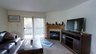 Located at 3220-3224 Mary St in Marinette, Wisconsin, this single-floor property offers a comfortable and functional layout designed for easy living. The living area serves as the heart of the space, anchored by a classic wood-mantled fireplace with a tile surround, adding warmth and a welcoming focal point to the room. Soft carpeting underfoot enhances the cozy atmosphere, while a large sliding glass door with vertical blinds floods the space with natural light and provides direct access to an outdoor balcony. The balcony overlooks a lush, tree-filled backdrop, offering a serene connection to the surrounding natural environment. The neutral wall tones and clean lines throughout give the space a calm, understated aesthetic that is easy to personalize. The living area comfortably accommodates a full entertainment setup alongside relaxed seating arrangements, making it well-suited for both everyday living and entertaining. The overall ambiance is relaxed and inviting, with thoughtful details that balance practicality and comfort throughout this Marinette property.