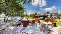 Located at 805 Canal St in Chattanooga, Tennessee, this thoughtfully designed outdoor courtyard serves as a central amenity space within a contemporary residential community. The grounds are generously landscaped with mature shade trees, ornamental grasses, flowering shrubs, and decorative rock beds that create a welcoming, resort-like atmosphere.

At the heart of the courtyard sits a circular brick fire pit surrounded by Adirondack-style chairs and plush lounge seating, making it an ideal gathering spot for residents. Adjacent to the fire pit is an outdoor kitchen station equipped with a built-in gas grill, accompanied by multiple dining tables and chairs for al fresco meals. A covered pergola structure provides a shaded retreat within the space.

Raised Corten steel planters filled with vibrant seasonal flowers add architectural interest and color throughout the grounds. Winding concrete pathways connect the various activity zones, encouraging exploration of the outdoor amenities. The space benefits from abundant natural light and open sky views, while mature trees provide cooling shade during warmer months.

The multi-story residential building frames the courtyard backdrop, featuring modern balconies and a mixed-material façade of brick and panel siding. The overall ambiance is one of relaxed, community-oriented outdoor living in the heart of Chattanooga.