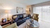 Located at 1403 Kirts Blvd in Troy, Michigan, this single-floor residence offers a thoughtfully designed layout with comfortable living spaces throughout. The living room provides a welcoming atmosphere with plush carpeting, large vertical-blind windows that invite natural light, and tasteful décor including framed artwork and a glass-top coffee table. Adjacent to the living area, the dining space is anchored by a ceiling fan with lighting and features sliding glass doors that open to outdoor views, creating a bright and airy environment. The galley-style kitchen is well-equipped with rich dark wood cabinetry, granite-style countertops, stainless steel appliances including a refrigerator, dishwasher, and microwave, and durable hardwood-style flooring. The residence includes multiple bedrooms, each featuring plush carpeting, large windows with vertical blinds for natural light and privacy, and accent walls that add depth and character. The full bathroom is finished with tile flooring, a tub-shower combination with glass doors, a rich wood vanity with an extended countertop, and clean white tile walls. The overall ambiance throughout the home is warm, neutral, and move-in ready.