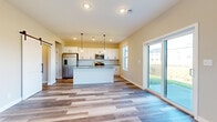 This two-story home is designed with a clean, modern aesthetic and a practical layout across both levels. The main floor centers on an open-concept kitchen and living area, where wide-plank wood-look flooring runs throughout. The kitchen is equipped with white shaker-style cabinetry, granite countertops, a central island, stainless steel appliances including a gas range, microwave, and French door refrigerator, complemented by a classic subway tile backsplash. Pendant lighting above the island adds a refined touch. Large sliding glass doors and multiple windows flood the living and dining areas with natural light and provide views of the surrounding neighborhood. A half bathroom on the main floor features a pedestal sink and hardwood-style flooring. The upper level is carpeted throughout and includes multiple bedrooms, each with generous windows that bring in abundant daylight. One bedroom features access to a spacious walk-in closet outfitted with wire shelving along all walls. A dedicated laundry room houses a full-size top-load washer and dryer with overhead wire shelving for added storage. A staircase with a dark wood handrail and carpeted treads connects both floors. The home features black hardware accents on doors and cabinetry, contributing to a cohesive, contemporary style throughout.