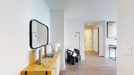 This thoughtfully designed single-floor residence blends modern aesthetics with functional living spaces, all finished to a high standard throughout. Warm wood-look flooring runs continuously across the unit, creating a cohesive and inviting atmosphere.

The entryway sets the tone with clean white walls, a sleek wooden credenza, a bold black-framed mirror, and curated accent lighting — offering an immediate sense of modern style. It opens into a well-organized corridor that connects the key living areas.

The kitchen is outfitted with two-tone cabinetry — high-gloss white uppers paired with natural wood-finish lowers — complemented by a herringbone-patterned tile backsplash and white countertops. Stainless steel appliances, including a full-size refrigerator and dishwasher, add a polished, professional touch.

The living room is a standout, featuring expansive floor-to-ceiling windows that frame sweeping panoramic views of the city skyline, green parkland, and open waterfront beyond. Natural light floods the space generously throughout the day.

The bedroom mirrors this quality with large corner windows offering equally impressive elevated views, creating a bright and airy retreat.

The bathroom is clean and contemporary, featuring hexagonal mosaic tile flooring, a floating wood-finish vanity with a white countertop, and a mirrored medicine cabinet.