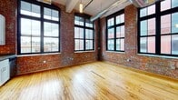 Located at 155 Clifford St in Providence, Rhode Island, this loft-style unit showcases the character of a beautifully converted industrial building. The open-plan living area is defined by warm hardwood floors, exposed brick walls, and soaring ceilings with visible ductwork that celebrate the building's historic industrial origins. Large, black-framed factory-style windows flood the space with abundant natural light while offering urban views of the surrounding Providence cityscape.

The kitchen is thoughtfully outfitted with white shaker cabinetry, dark stone countertops, and a full suite of stainless steel appliances including a refrigerator, electric range, dishwasher, and over-range ventilation hood. The kitchen opens naturally toward the main living area, reinforcing the loft's open and airy feel.

The bathroom features a clean, modern finish with white subway tile in the walk-in shower, a single vanity with stone-tone countertop and white cabinetry, a medicine cabinet with mirror, and tile flooring. In-unit laundry is also present, adding everyday convenience.

Throughout the space, the interplay of raw brick, warm wood, and modern finishes creates a distinctive industrial-chic ambiance, making this Providence loft a compelling blend of historic character and contemporary comfort.