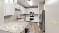 Located at 25 Station Ct in Greenville, SC, this two-bedroom, two-bathroom residence offers a thoughtfully designed single-floor layout with a generous overall footprint. The kitchen is a standout feature, showcasing white shaker cabinetry, granite countertops, a classic subway tile backsplash, a stainless steel undermount sink, and a full suite of stainless steel appliances including a range, built-in microwave, dishwasher, and refrigerator. Wood-look flooring grounds the kitchen and flows into the adjacent living area, which is carpeted and benefits from natural light and sliding door access to a private balcony. Both bedrooms are carpeted and equipped with ceiling fans. The primary bedroom is notably spacious, featuring a large walk-in closet with wire shelving. The second bedroom includes a wide window with outdoor views. Each bathroom is finished with granite-topped white vanities and a tub-shower combination. The primary bath features a dual-sink vanity with a large framed mirror, while the secondary bath offers a single vanity. Wood-look flooring continues throughout both bathrooms. The residence also includes two closets, providing ample storage throughout.