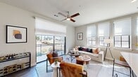This thoughtfully designed single-floor residence offers a bright, open-concept layout that seamlessly connects the living, dining, and kitchen areas. The living room is anchored by large floor-to-ceiling sliding glass doors that open to a private balcony, flooding the space with natural light and providing open outdoor views. A ceiling fan overhead and multiple additional windows on the adjacent wall further enhance the airy atmosphere. Durable wood-look flooring runs throughout the main living areas, complementing the contemporary neutral palette.

The kitchen features dark cabinetry paired with a generous quartz waterfall island, complete with a deep undermount sink and bar seating — an ideal space for both cooking and casual dining. The open sightlines from the kitchen to the living area reinforce the spacious, connected feel of the home.

The bedroom is carpeted for comfort and benefits from its own set of large windows, offering natural light and outdoor views. A bold upholstered headboard wall and direct access to a walk-in closet add both style and practicality.

The bathroom is finished with large-format marble-look tile on both the walls and floor, a soaking tub with integrated shower, and dark wood cabinetry topped with a white quartz vanity. A dedicated in-unit laundry area with a full-size washer and dryer completes this well-appointed residence.